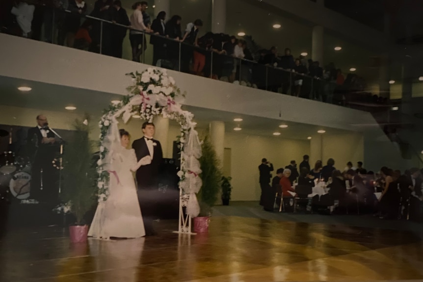 A photograph showing a couple in front of an arch with an audience watching.