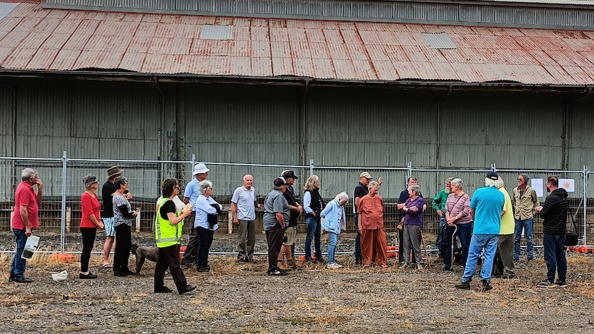 People stand in front of a corrugated iron shed. 