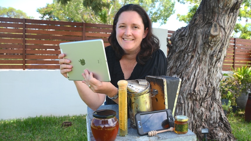 a  woman in  backyard with old honey making equipment and an electronic tablet, mobile phone on a old bee hive