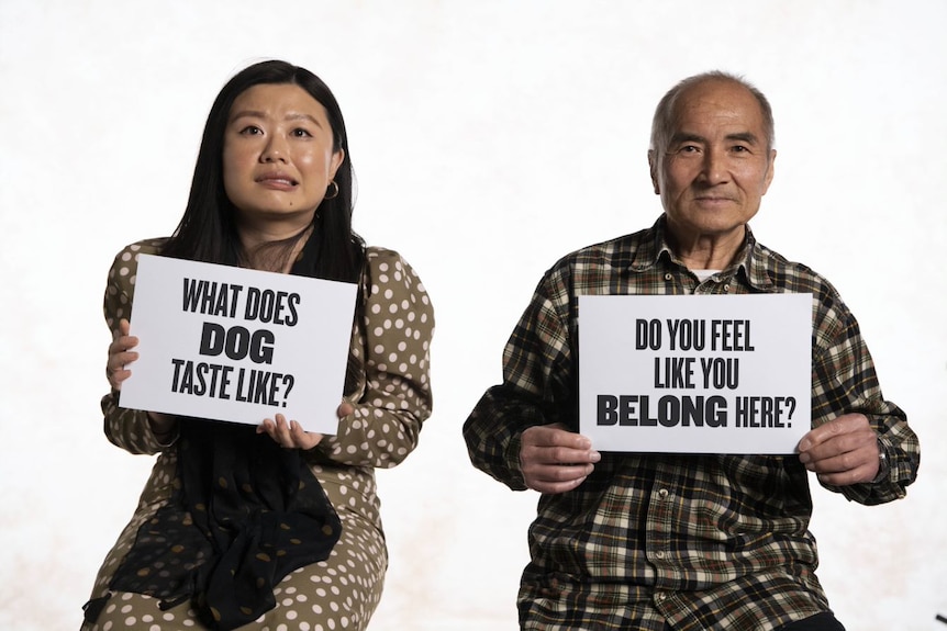 Cindy Tan and Douglas Lam hold placards of "What does dog taste like?" and "Do you feel like you belong here?"