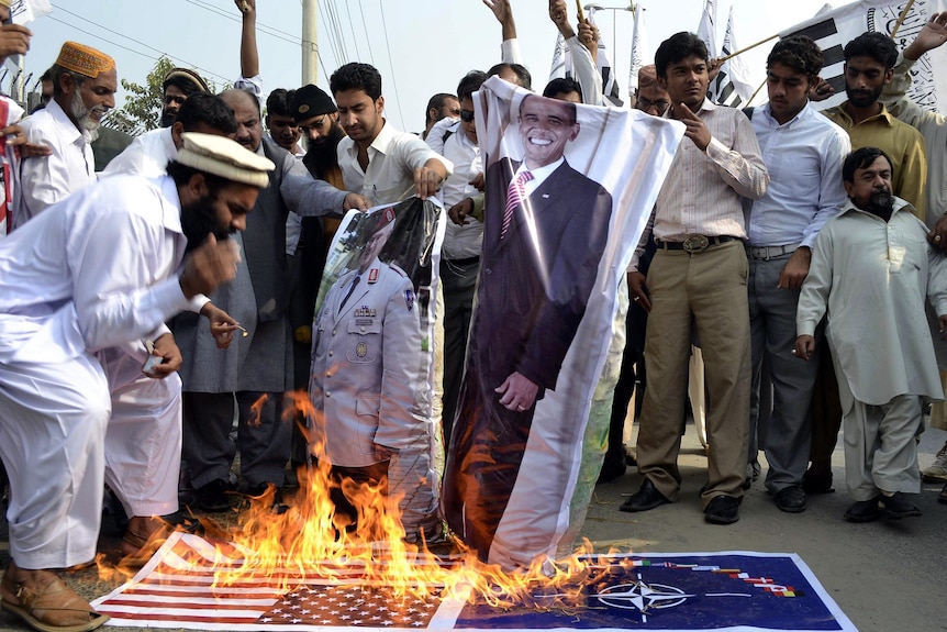 Pakistanis burn an effigy of US President Barack Obama, NATO and US flags.