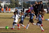 Unidentified children running after ball during soccer match at Harrison district playing fields in Canberra