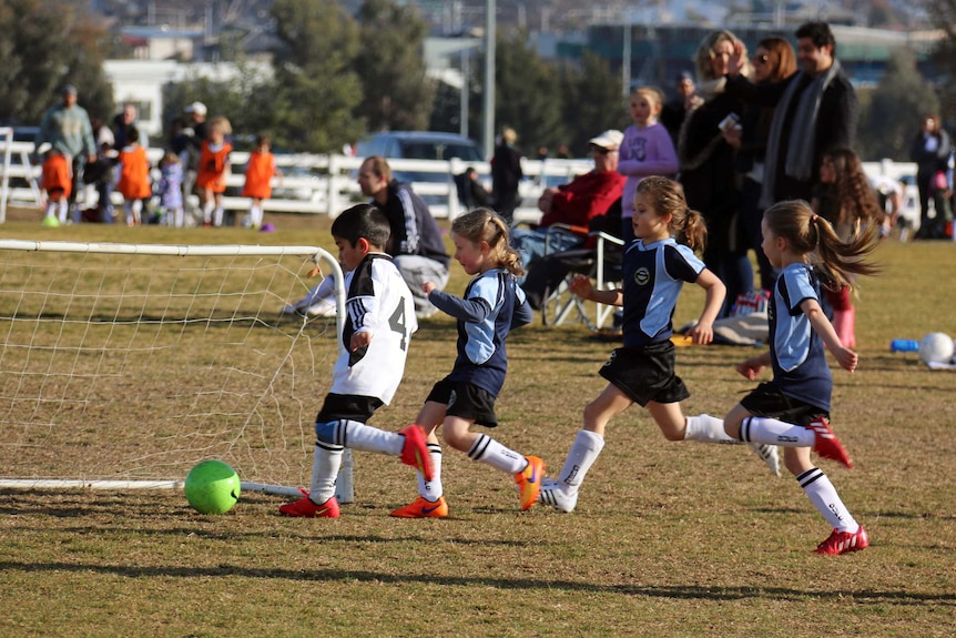 Unidentified children running after ball during soccer match at Harrison district playing fields in Canberra