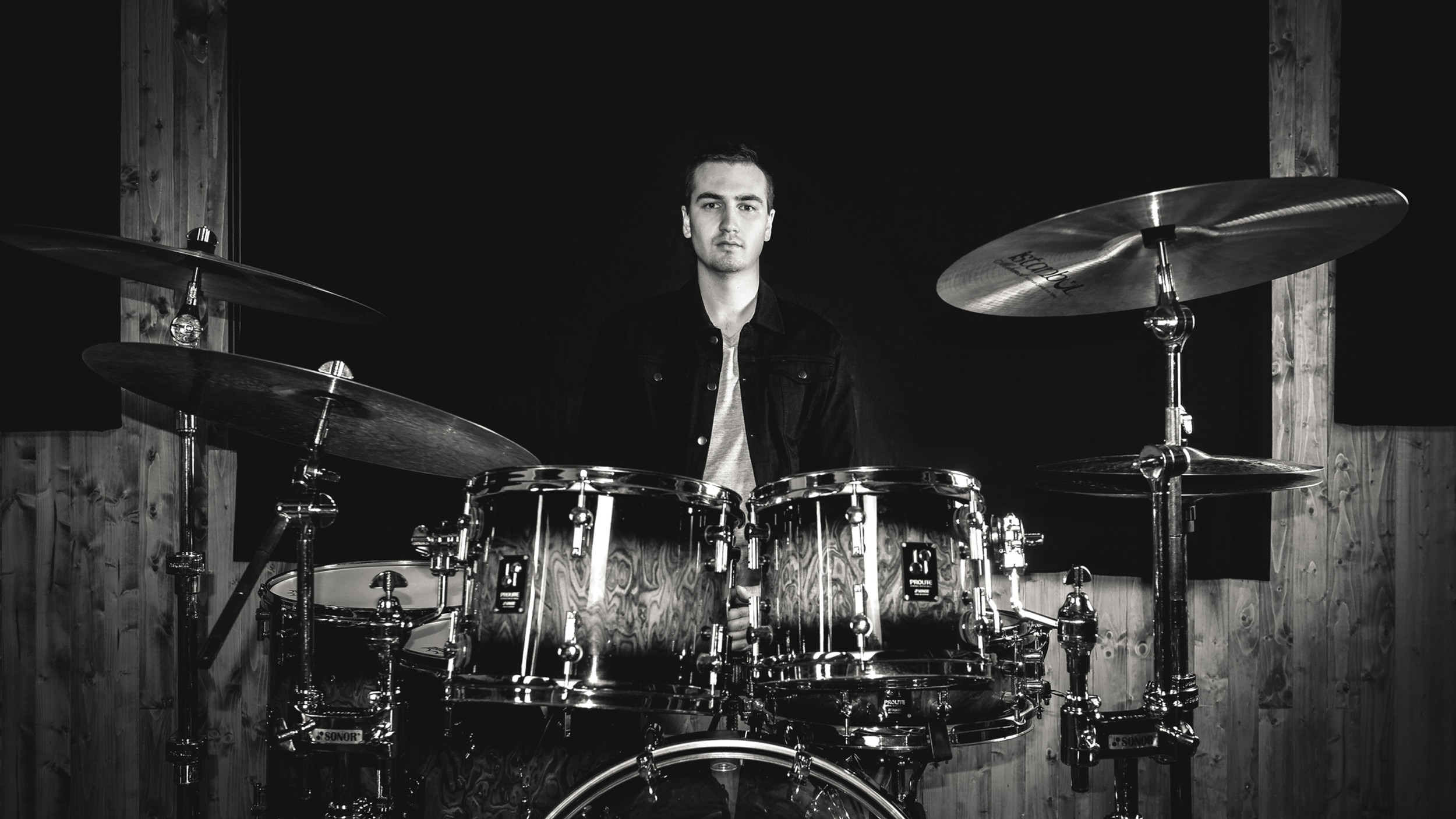 A monochrome photo of Will Régnier at his drum kit looking at the camera
