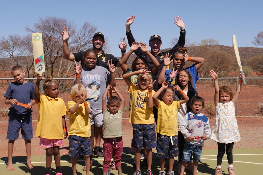 Young cricketers and coaches raising their arms happily out in the desert.