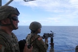 Two soldiers in camouflage gear on a US vessel and looking out to sea.