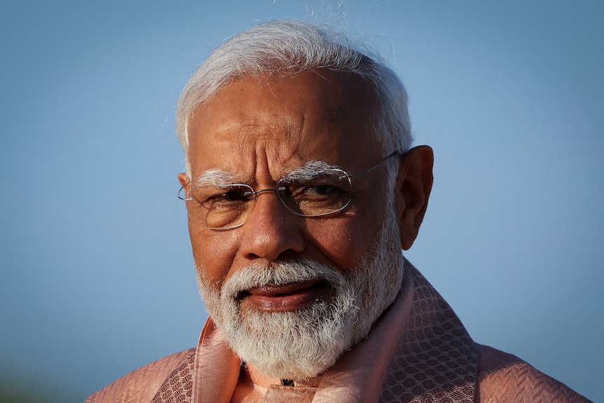 Narendra Modi pictured against a pale blue sky, squinting through his glasses