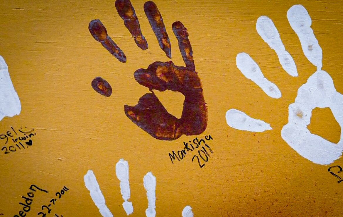 A handprint on an orange wall with Markisha 2011 written underneath.
