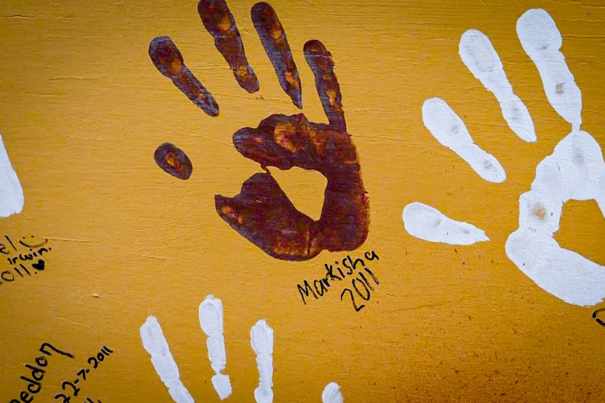 A handprint on an orange wall with Markisha 2011 written underneath.