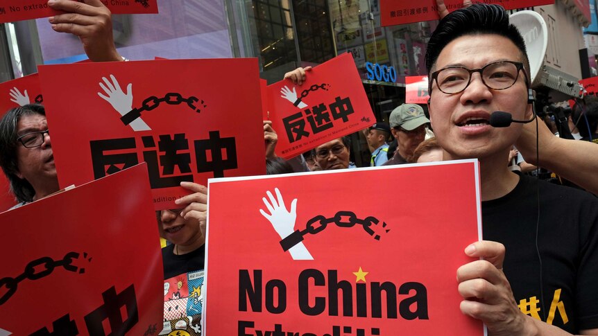 A crowd of people are photographed close-up, holding red placards that read 'No China Extradition' with a logo of a hand cuffed.