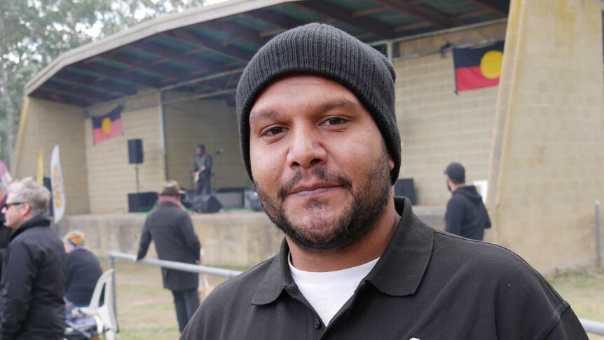 A man in a rangers uniform poses outside a building adorned with Aboriginal flags in a nature reserve