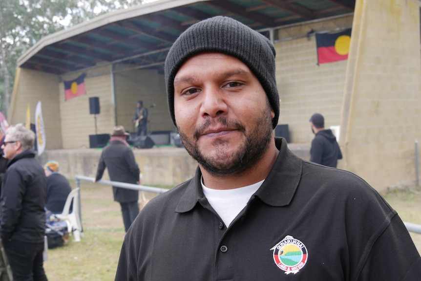 A man in a rangers uniform poses outside a building adorned with Aboriginal flags in a nature reserve