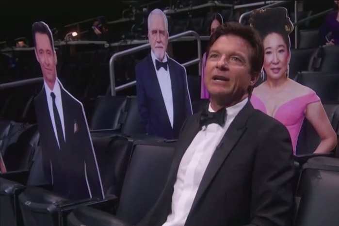 Jason Bateman at the Emmys sitting amongst cardboard cut-outs of other actors.