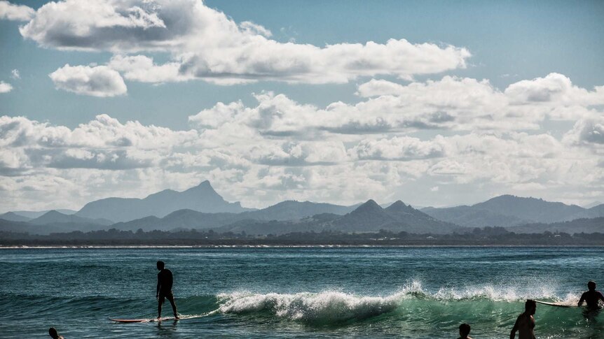 A landscape photo of a man surfing in front of mountains