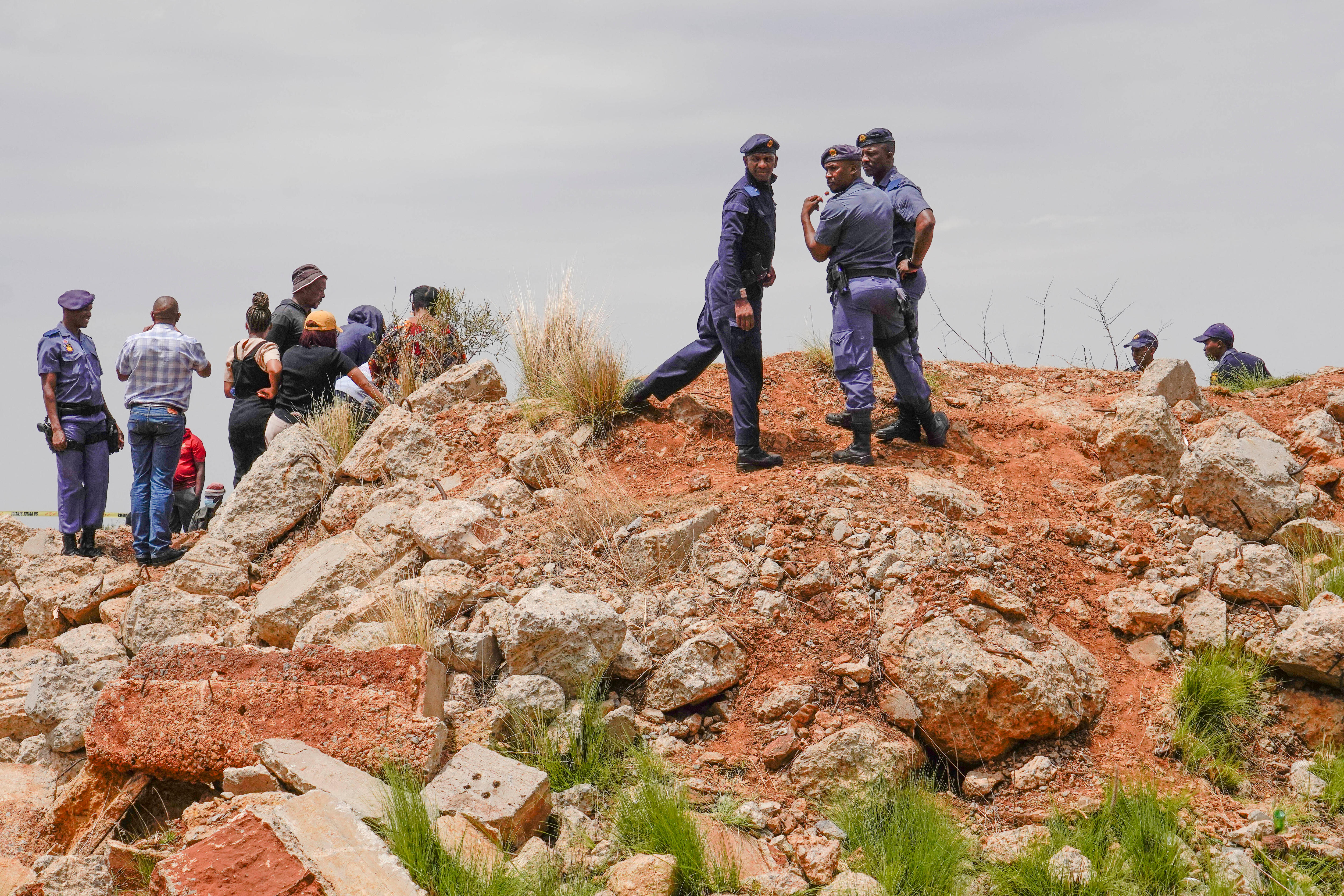 Police officers and volunteer rescuers stand by the opening of a gold mineshaft.