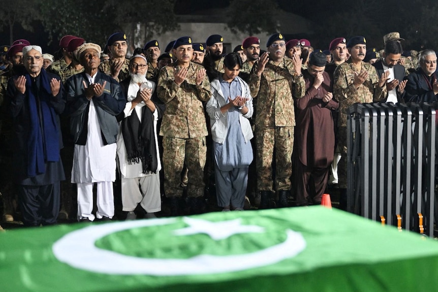 Politician and military dignities pray in front of a coffin draped in a Pakistan flag 