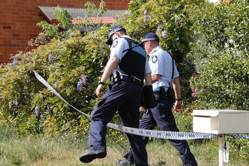 Two officers cross a police tape line.