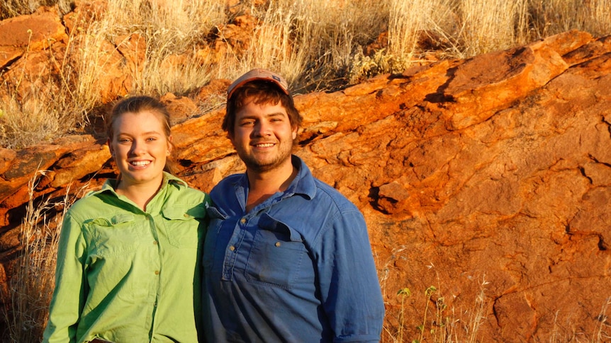 A Woman and man standing in front of red rock with dry grass in it.