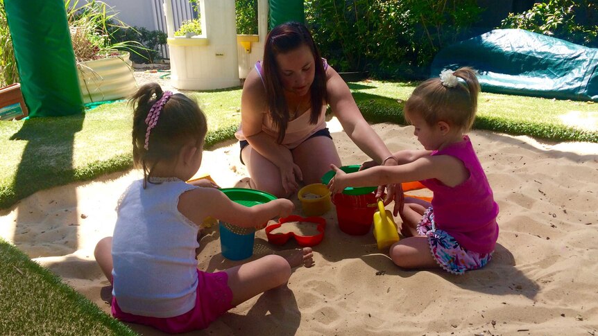 Emily Bills plays with two of her three daughters in a sand pit.