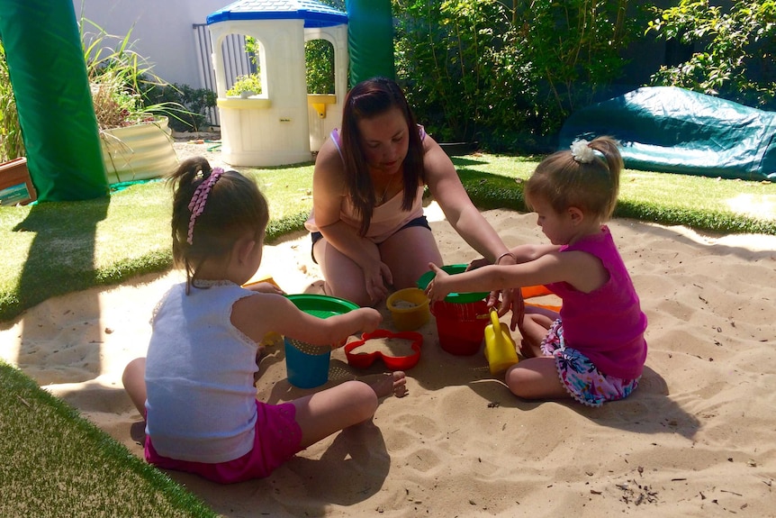 Emily Bills plays with two of her three daughters in a sand pit.