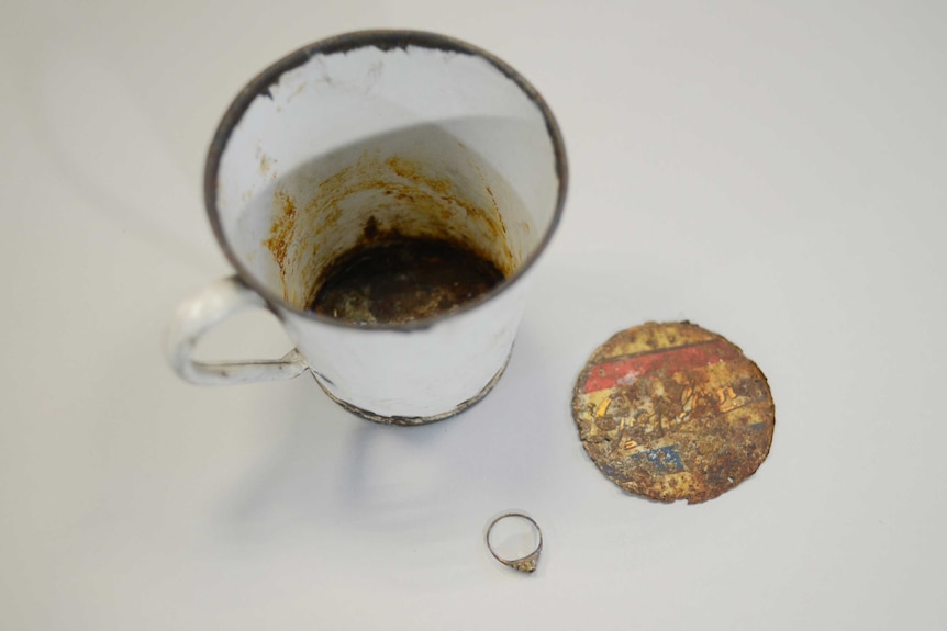 A gold ring and the mug it was found in sit on a table.