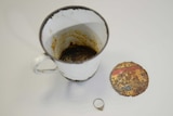 A gold ring and the mug it was found in sit on a table.