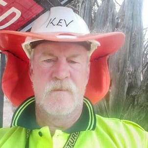 A man wears a yellow high-vis shirt and a helmet with the name 'Kev'.
