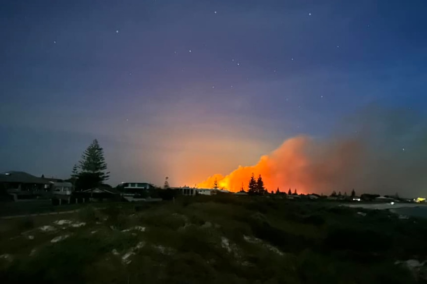 A fire burns in the near distance at sunset