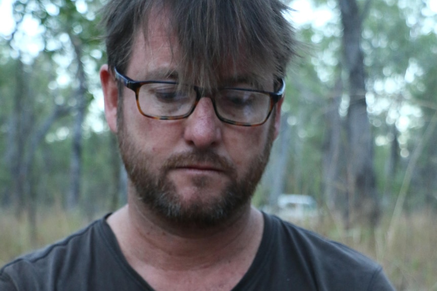 A man with glasses holds a small marsupial in his hands