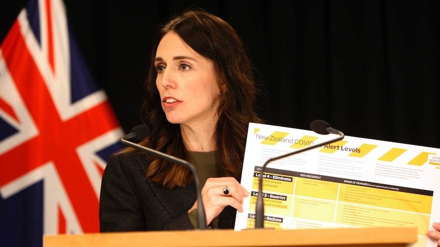 Jacinda Ardern holds up a poster explaining New Zealand's coronavirus alert system