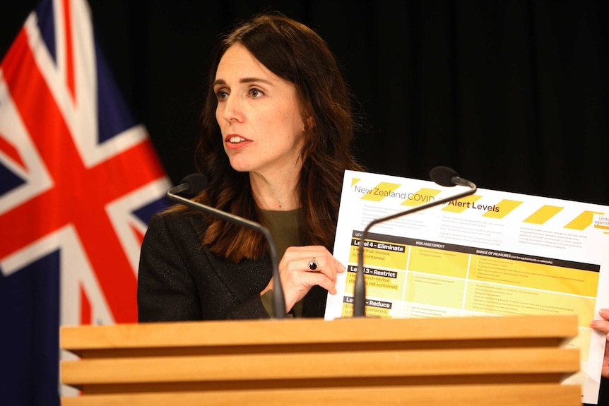 Jacinda Ardern holds up a poster explaining New Zealand's coronavirus alert system