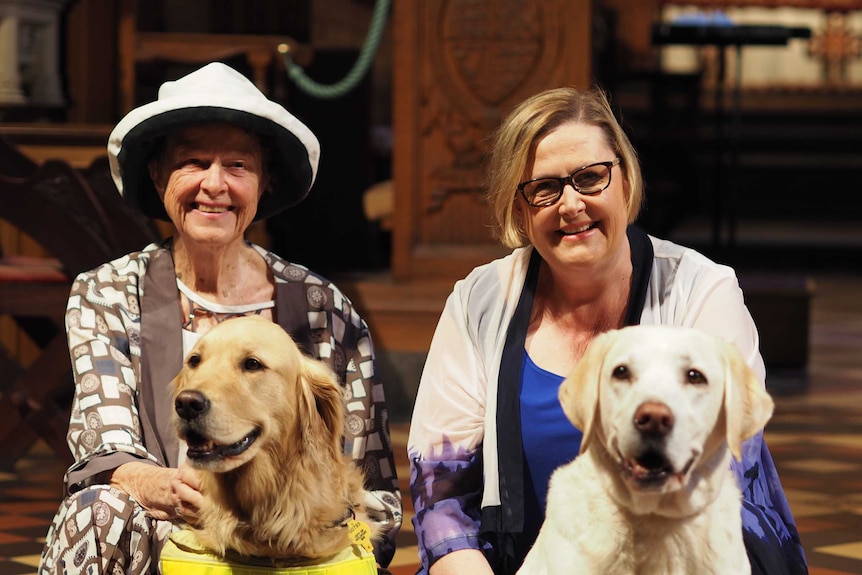 Two women sit down with two dogs.