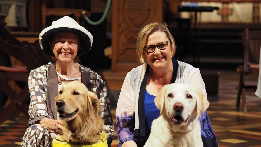 Two women sit down with two dogs.