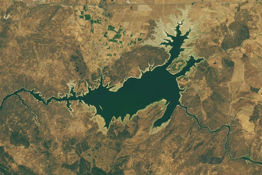 A satellite map of a lake region of Spain, with dark blue water and narrow sandy-looking borders around the water.