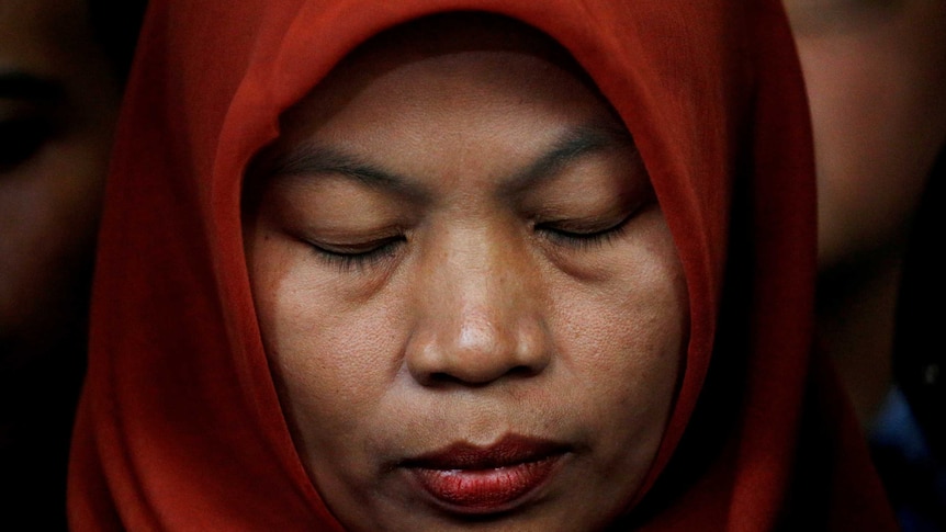 Baiq Nuril Maknun stands with her eyes closed wearing an orange hijab at a press conference.