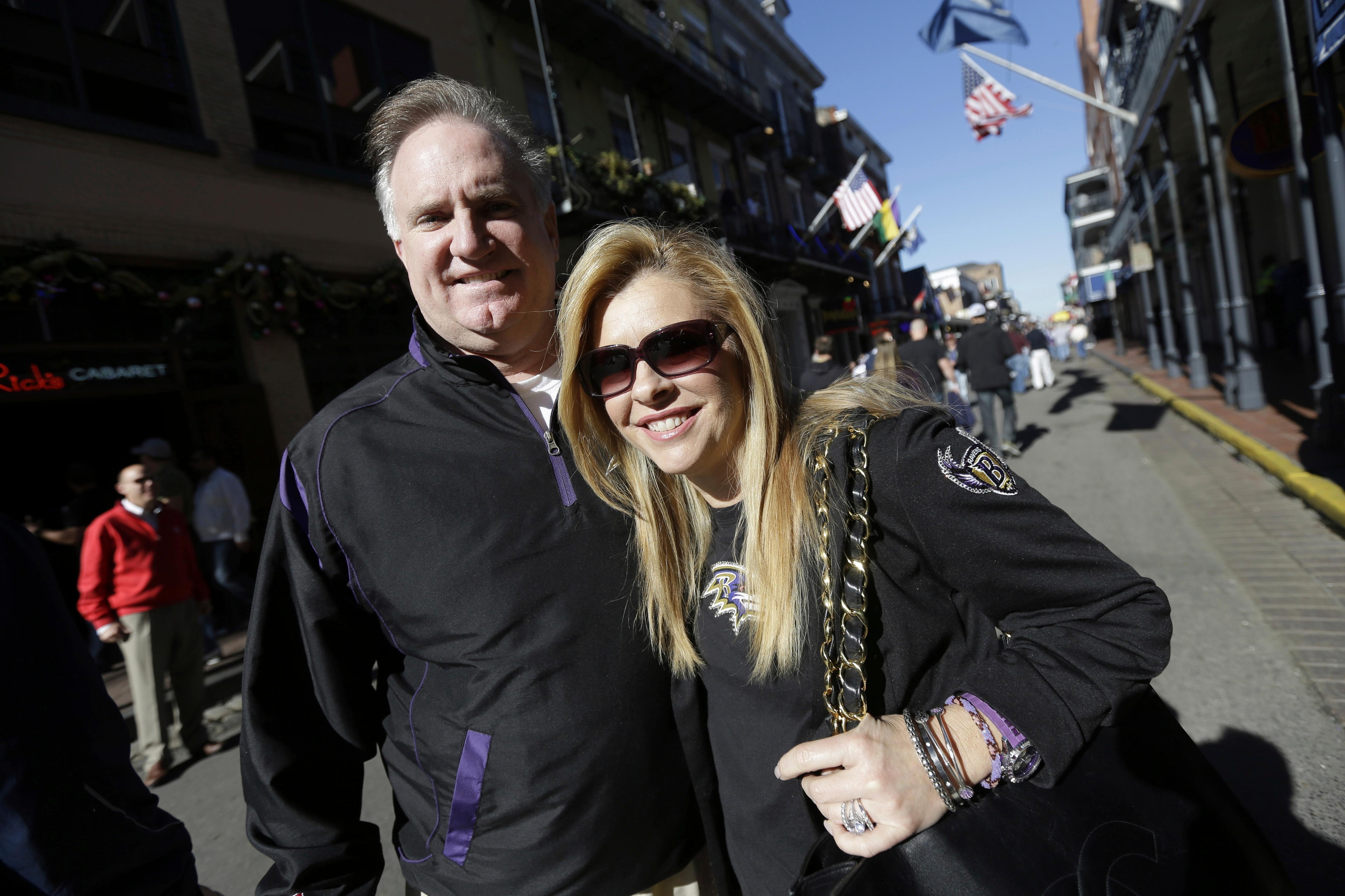 A man and a woman wearing black ourfits huggin and smiling for camera outside in the sun.