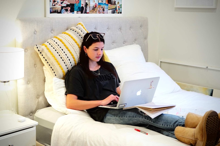 Alexia Osler uses a laptop while sitting on her bed.