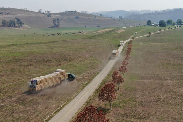 A trucked loaded with hay bales is parked alongside a country road with rolling hills in the distance.