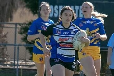 A woman wearing a blue and white guernsey runs with a ball under her arm