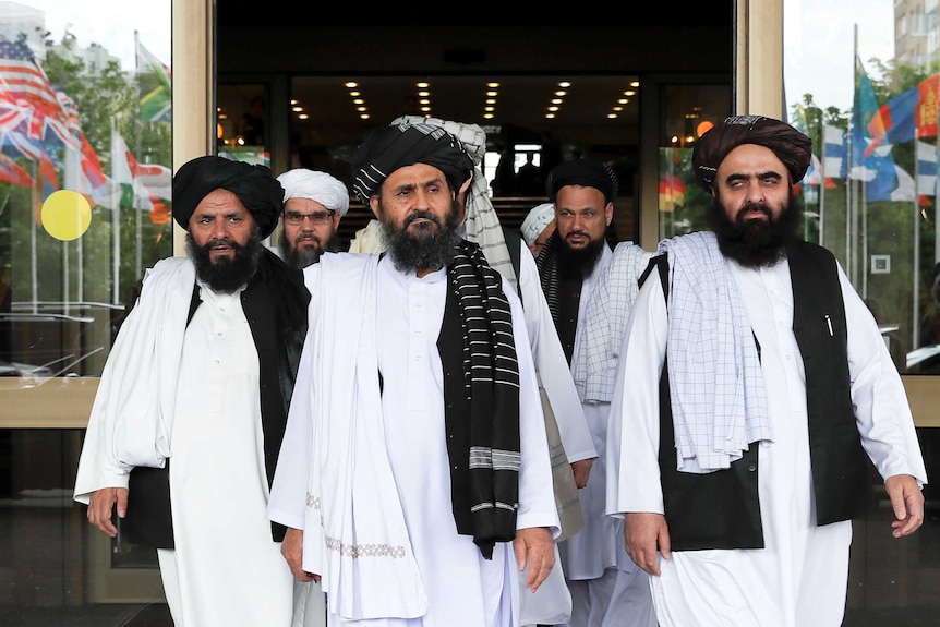 Men in white robes with headwear leave a building.