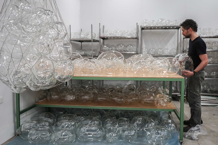 A man stands with bubbles of different shapes and sizes covering a table and several shelves.