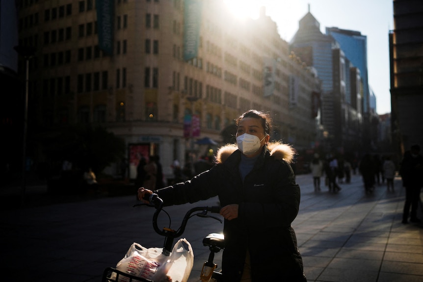 A woman wearing a protective mask walks with a bike in China.