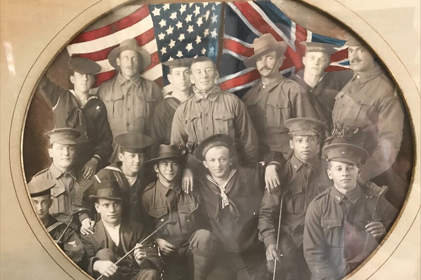 A sepia photo of 14 Allied men in World War 1 in uniform against a colorised American and British flag