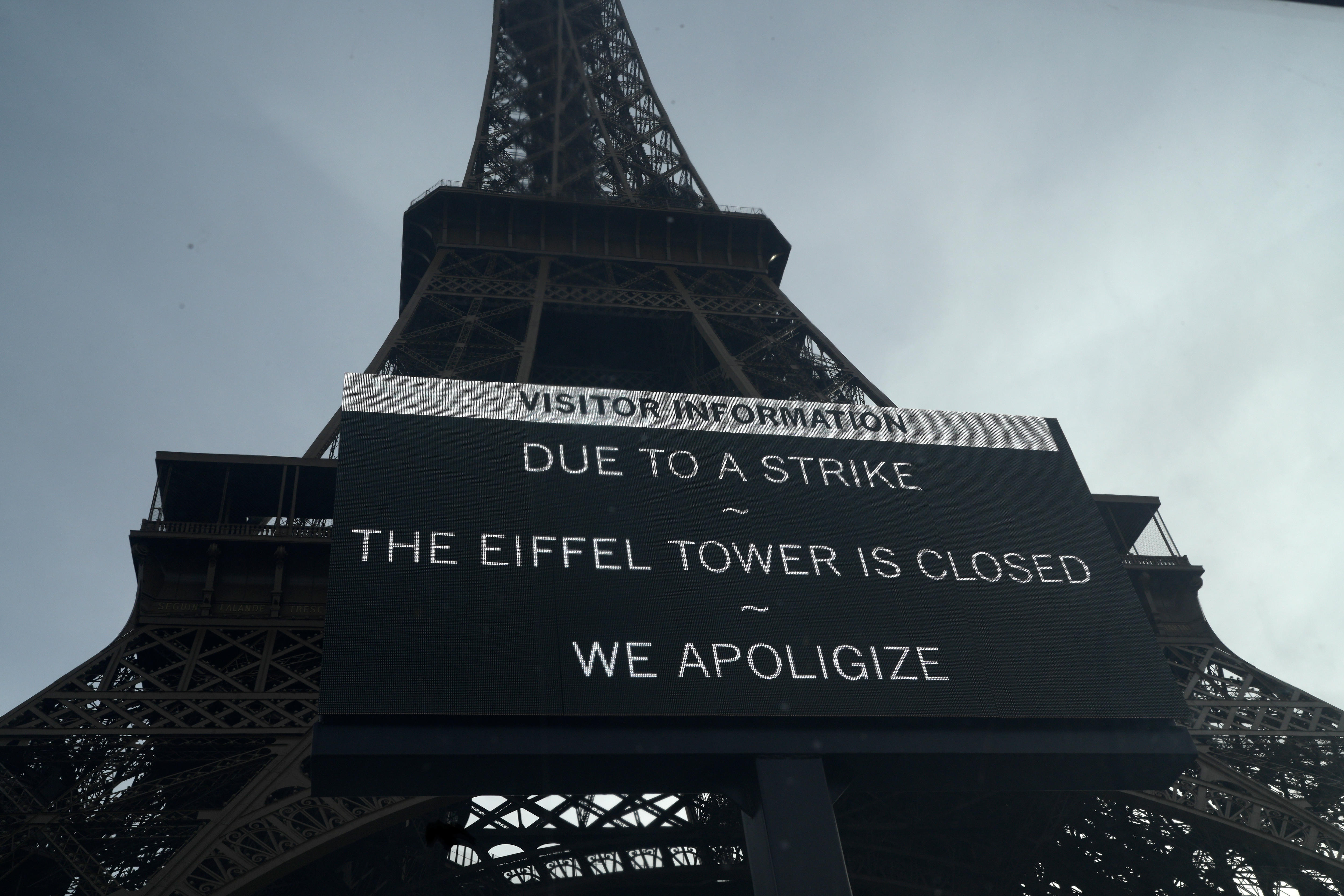 A board in front of the Eiffel Tower warns about a strike. "Due to a strike, the Eiffel Tower is closed. We spologize," it says.
