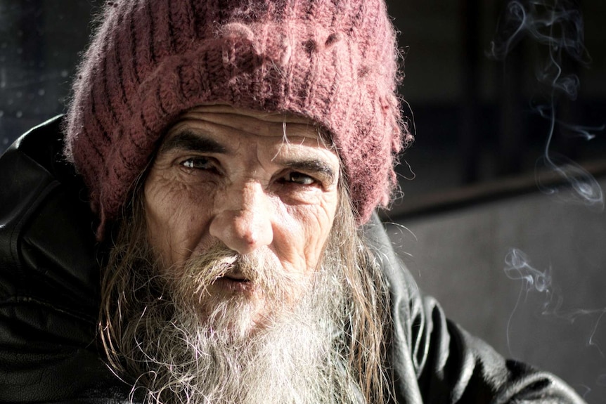 A man with a pink beanie and long grey beard looks forward.