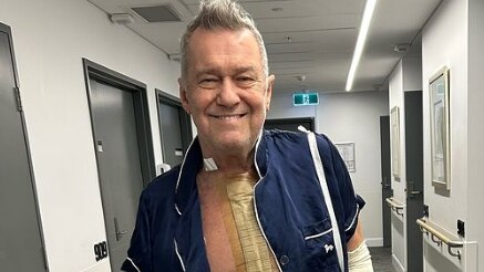A man stands smiling while wearing a hospital gown.