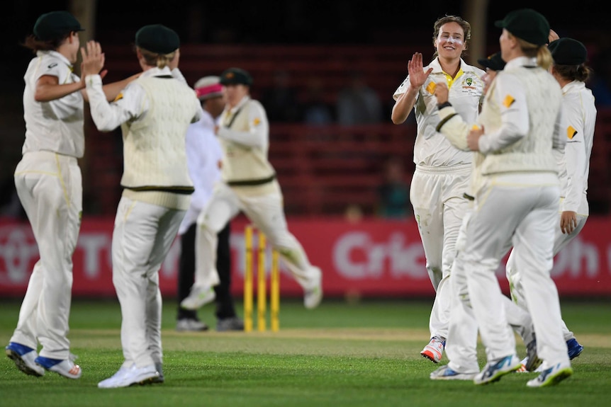 Female cricket players in Australian Test uniforms celebrate on the pitch.