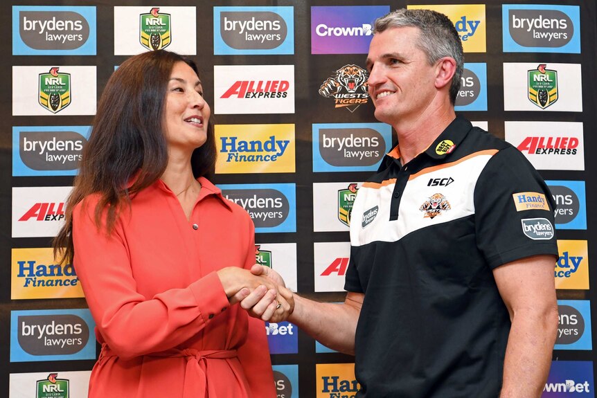 Marino Go and Ivan Cleary smile while shaking hands in front of an advertising board.