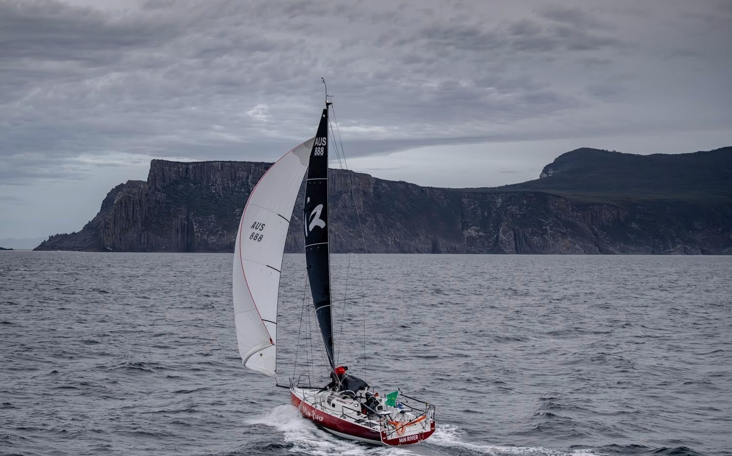 Un yate con velas blancas y negras navegando a lo largo de una espectacular costa.