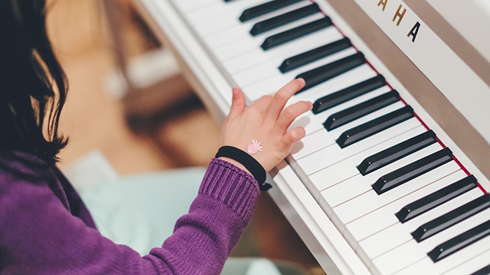 A child presses down on an upright piano keyboard with one finger. She wears a purple jumper.